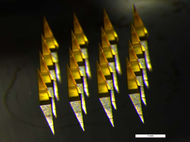 columns of illuminated microneedles, glowing yellow, reflected on a shiny surface