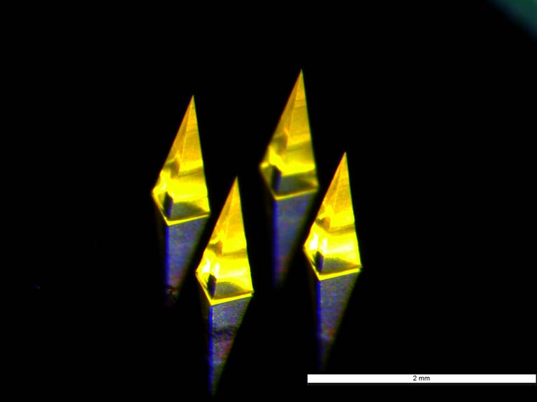 four glowing pyramid-shaped microneedles on a reflective surface