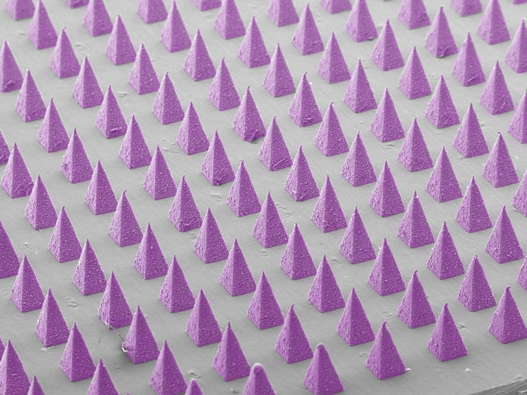 angled view from above of dozens of sharp purple pyramids laid out in a grid on a gray base