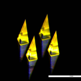 four glowing pyramid-shaped microneedles on a reflective surface