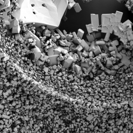 Black and white image of a pile of small square crystals, with bigger crystals loosely arranged across the top. Almost like a seismic wave going through the Earth's crust.