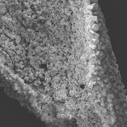 Black and white image of a pile of small square crystals, placed diagonally with a black background. The crystallization looks like a geode in form.